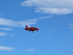 Fotka zachycuje jeden letoun BAE Hawk T1 britské skupiny Red Arrows s vysunutým podvozkem, pravděpodobně při příletu, odletu nebo dynamické ukázce.